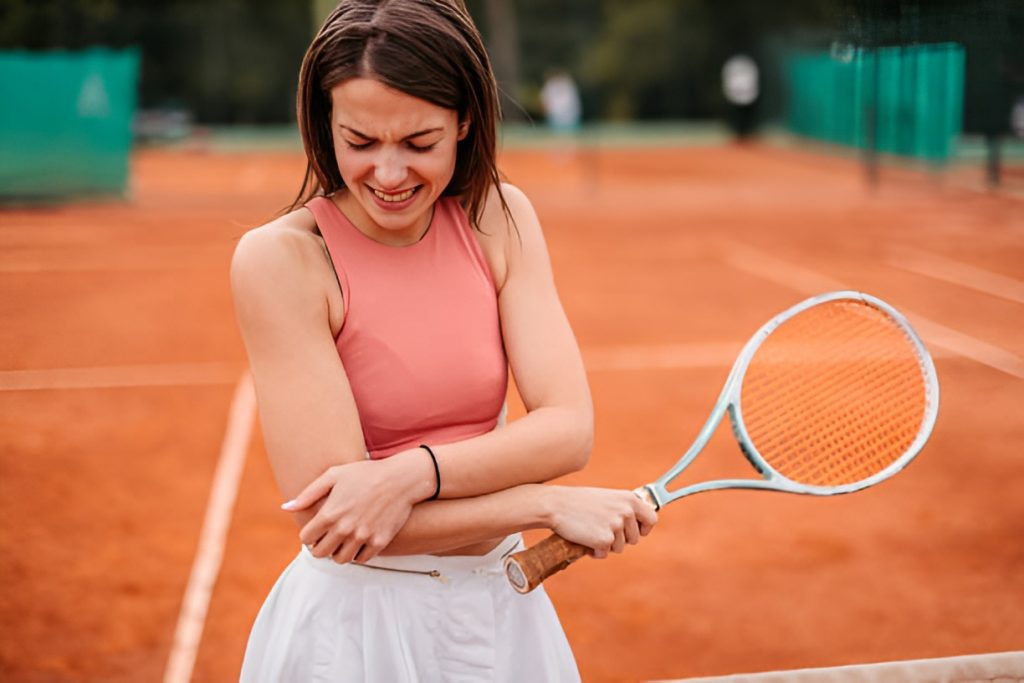 woman holding a tennis racket, wincing in pain while squeezing her arm