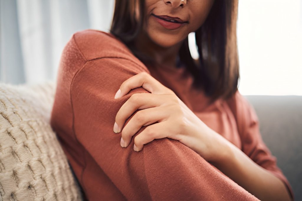 woman in a brown sweater squeezing her arm